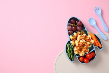 Colorful children lunch served in a blue rocket-shaped plate. Balanced meal includes grapes, waffles, cherry tomatoes, carrots, and green cucumber
