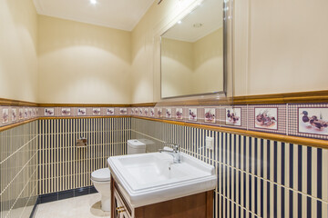 The interior of the bathroom, decorated in an elegant English style. The lower part of the wall is decorated with white and blue tiles with a beautiful border.