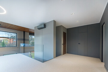 A spacious hall with doors in a high-tech country house. Glass railings on the second floor. Panoramic Windows with a beautiful view.