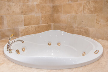 Corner bathtub with hydromassage in the interior, decorated in a Mediterranean style with beige tiles. Stylish mixer.