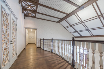 The hall of the second floor of a luxurious country mansion. Railings with wooden balusters, doors with an exquisite pattern, beautiful ceiling beams.