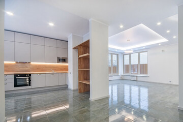 White kitchen set with built-in appliances in the interior of a luxury country house. Grey 
floor tiles, spotlights and large windows.