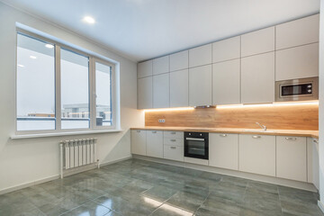 Elegant kitchen design with a large window. White kitchen set with built-in appliances. 
The countertop and apron of the headset are decorated with light wood.