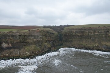 Coastal waterfall plunging into sea from cliffs between Scarborough and Whitby aerial panorama landscape view,United Kingdom Scotland