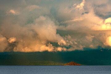 A small island emerges from Lake Villarrica in Chile's Araucanía Region, set against a dramatic, cloudy sky.
