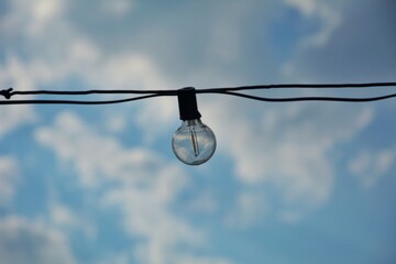 Obraz premium Hanging Light Bulb on Wire with Clear Blue Sky