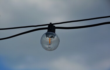 Vintage Light Bulb Hanging on Cable Against Cloudy Sky