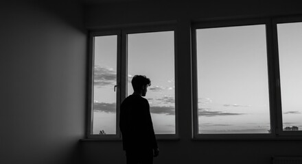Man standing by window gazing at sunset with copy space  