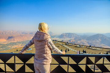 Blonde tourist admiring the breathtaking panorama of AlUla Old Town and surrounding desert landscapes from Harrat Viewpoint in Saudi Arabia