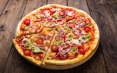 Pizza on wood background, with onions, bacon and cherry tomatoes, thin pastry crust, closeup