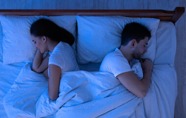 Young Spouses Sleeping Lying Back-To-Back In Bed In Bedroom At Night. Above View, Low Light