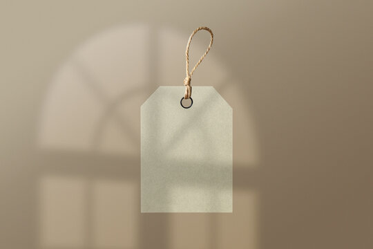 A blank, light-colored tag with a string hanging against a soft, blurred background resembling a window shadow. Ideal for labeling or branding purposes.