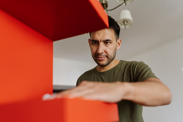 Close-up portrait of young man wiping dry red surface of shelf with white paper towel after housekeeping at home, close-up. Concept of cleanliness and hygiene in domestic environment.
