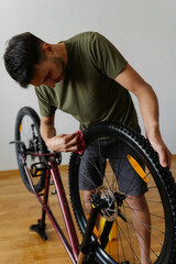 Vertical portrait of focused cyclist cleaning dusty dirty tire of bicycle wheel with cloth, detailing bicycle at home during cycling maintenance and equipment care. Concept of bike service.