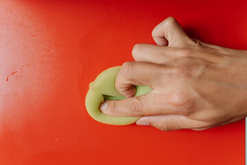 Close-up cropped shot of unrecognizable man using cleaning cloth, wiping dusty dirty red shelf showcasing commitment to cleanliness and hygiene. Concept of domestic work, housekeeping, household.
