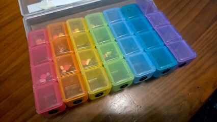 Weekly pill organizer with color-coded compartments on wooden surface