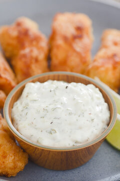 Fresh homemade tartar sauce made of mayonnaise, pickles, capers, herbs, salt and pepper, with fried fish fillet pieces on the side (Selective Focus, Focus on the front of the sauce)