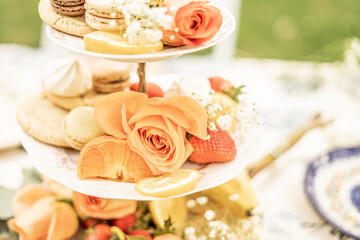 tiered dessert stand decorated with assorted macarons, sliced citrus fruit, strawberries, and fresh orange roses, styled for an outdoor garden tea party