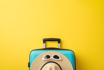A blue suitcase with summer travel accessories like a straw hat and sunglasses placed on it,...