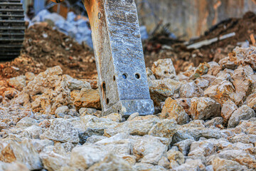 Close-up of a hydraulic rock breaker hammer crushing large stones at a construction site. Heavy-duty machinery used for demolition and excavation work in rugged environments