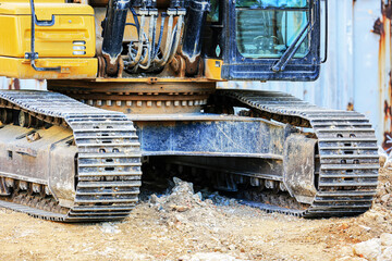 Low-angle view of an excavator’s crawler tracks and base section at a construction site. Rugged steel treads designed for mobility and stability on uneven terrain and loose dirt