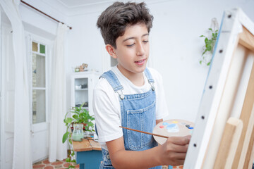 Smiling boy painting on canvas in bright cozy art room