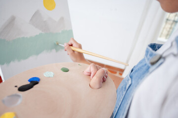 Boy painting mountain scene with acrylics and wooden palette