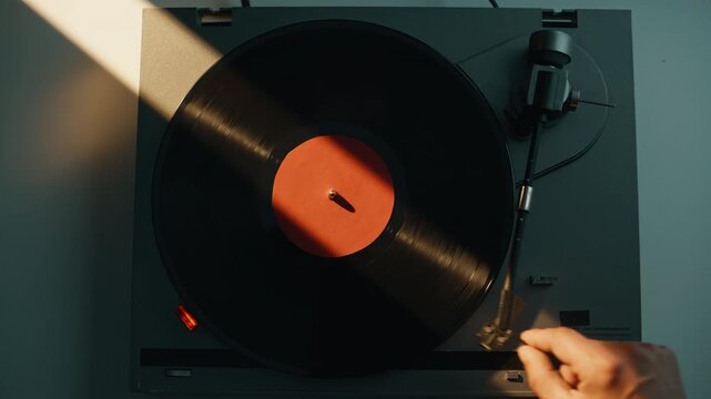 Hand putting gramophone needle on black vinyl disc in evening light closeup.
