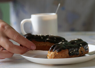 Delicious eclair dessert and coffee - Hand Reaching for a Decadent Chocolate Eclair on a Plate with...