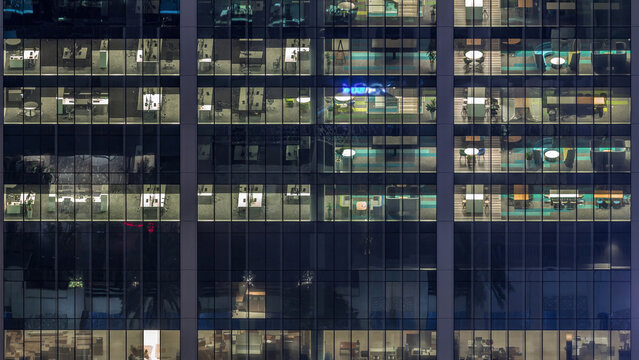 Office building exterior during late evening with interior lights on and people working inside night timelapse