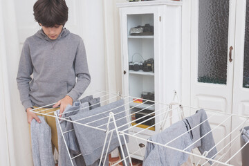 Teen boy hanging clean clothes on indoor drying rack