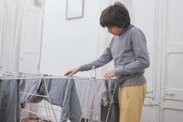 Teen boy doing laundry and hanging clothes at home