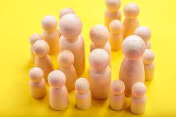 Wooden peg people figures on yellow background: family and community concept