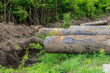 Fototapeta premium Old rusty metal pipes outdoors on soil next to lush green field