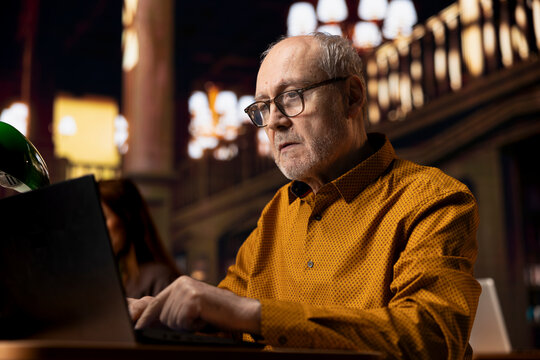 College campus library with a mature student researching a thesis project, demonstrating inspiration and dedication required for adult academic success. Old man working on his paperwork.