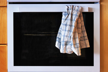 The front view of a white kitchen oven with control knobs and a plaid kitchen towel hanging from...