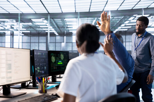 Engineer doing high five gesture with colleague after receiving access granted notification while reconfiguring server hub. Data center staff members celebrating successfully eliminating all errors