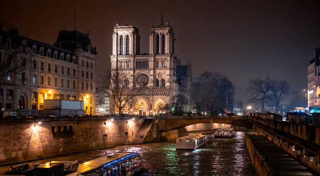 Notre-Dame de Paris illuminated at night with boats cruising on the Seine river, winter cityscape and reflections. Notre-Dame, Notre Dame, Paris, Seine, cathedral, France