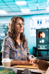 Senior woman patient meeting with her doctor to discuss results in an office, using advanced tools...