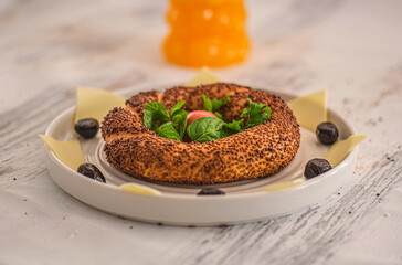 Traditional Turkish simit (sesame bagel) beautifully arranged on a white plate. Presented on a rustic white wooden table. Selective focus.
