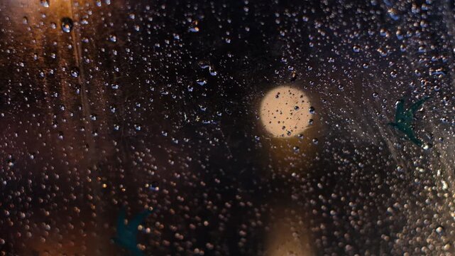 A blurry image of a city street with raindrops on the window. Scene is somewhat melancholic, as the rain and blurred cityscape create a sense of isolation and detachment