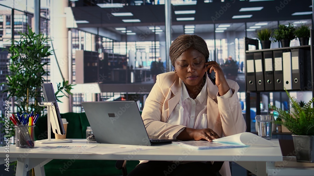 Poster african american general manager answers smartphone call to discuss performance metrics, focusing on