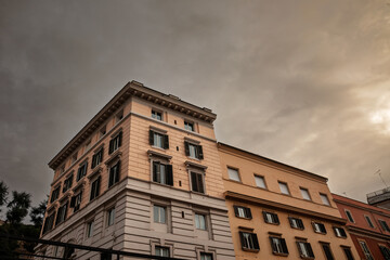 Oblique view of a late 19th‑century Roman apartment block with cream and ochre facades, shuttered windows and decorative cornices, silhouetted against a dramatic evening sky in the historic center.