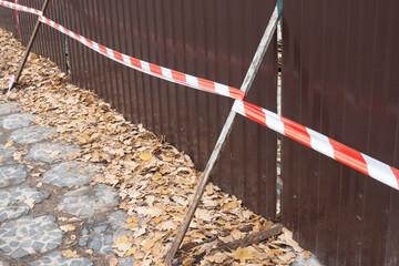 Safety barriers cordon off a construction area along an urban pathway, with scattered leaves...