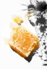 Honey in honeycombs dripping, pouring from glass honey dipper spoon, on white background with shadows. Healthy organic liquid honey spill, with flowers. Flat lay, top view, from above vertical shot 