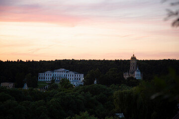 Fototapeta premium Beautiful sunset sky and tree, branch, bush on silhouette on colorful clouds from the high hill down on forest, park, architecture building. Nature in the evening time at summer. Natural real colors