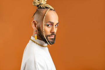 Confident black gay man with bright makeup standing isolated on orange background, dressed white. Exudes sense of pride and individuality. Diversity power of personal style