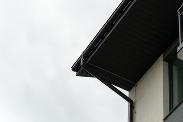 Cloudy sky looms over the roof edge of a modern building, showcasing a sleek rain gutter design....