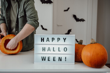 happy halloween neon sign on the table near pumpkin with man carving lantern, copy space banner
