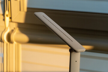 Soft sunlight bathes a sleek, minimalist desk lamp positioned by a window, highlighting its elegant...